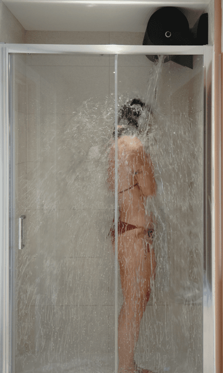 Female standing under the cold drench and being covered in falling water